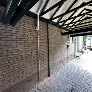 Een airco-installatie met een witte aansluitbuis aan de wand voor binnen- en buitenunits.