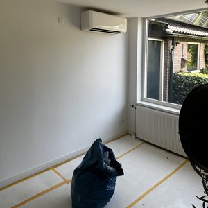 Een wandmodel airconditioningseenheid geïnstalleerd in een lichte kamer met uitzicht naar buiten.