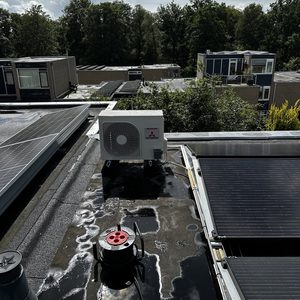 Deze afbeelding toont een airco-installatie op een dak, omringd door zonnepanelen en andere apparatuur.