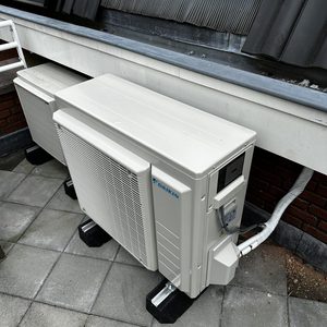 Buitenunit van een Daikin airconditioning systeem, geplaatst op een tegelvloer met zichtbare installatiebasis.