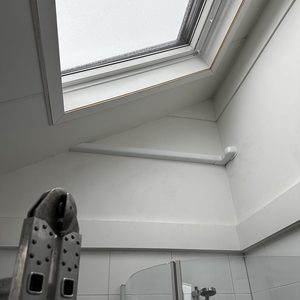 Een airconditioninginstallatie in een vernieuwde ruimte met een hellend dak en een ventilatiebuis zichtbaar aan de muur.