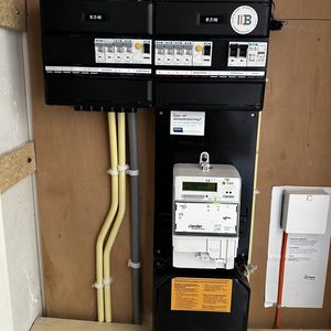 De foto toont een meterkast met elektriciteitsmeter en automatische zekeringen, zorgvuldig geïnstalleerd met kleurgecodeerde bedrading.