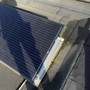 Installatie van zonnepanelen op een dak, met schaduwen zichtbaar van personen. De panelen zijn op een verhoogde constructie geplaatst.