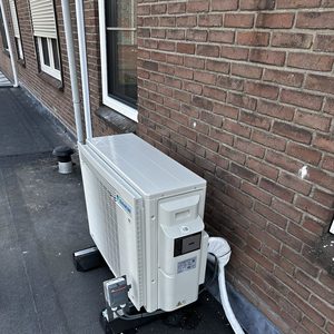 De afbeelding toont een buitenunit van een airconditioning systeem, die stevig is bevestigd aan een muur, met duidelijk zichtbare leidingen en een nette afwerking.