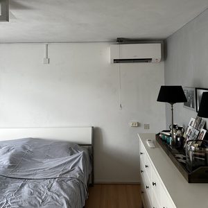 De afbeelding toont een wand-airconditioner geïnstalleerd in een slaapkamer, met een minimalistisch interieur en een bed zichtbaar op de voorgrond.