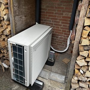 Een buitenunit van een airconditioningsysteem geplaatst in een afgesloten ruimte, omringd door houten stapels.