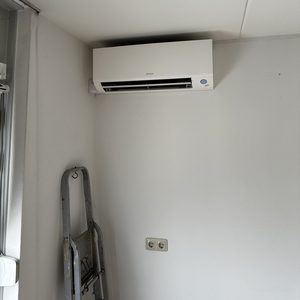 Een wandmodel airconditioner is geïnstalleerd in een binnenruimte, met een ladder in de buurt voor installatie- of onderhoudswerkzaamheden.