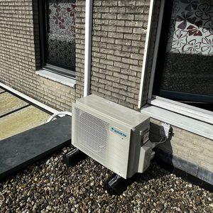 Een buitenunit van een Daikin airco-installatie, geplaatst op een zwarte basis en omgeven door grind.