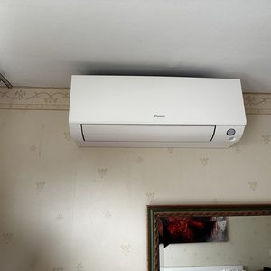 Een wandmontage airconditioningseenheid van het merk Daikin, geïnstalleerd in een interieur met een neutrale wand en een spiegel.