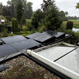 Installatie van zonnepanelen op een hellend dak, zichtbaar zijn meerdere panelen met natte oppervlakken door de regen.