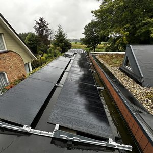 De afbeelding toont zonnepanelen die op een hellend dak zijn geïnstalleerd. Het oppervlak is nat, wat wijst op recent neerslag.
