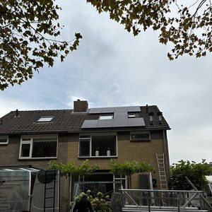 Op het dak worden zonnepanelen geïnstalleerd, met een werknemer die materialen voorbereidt voor de installatie.