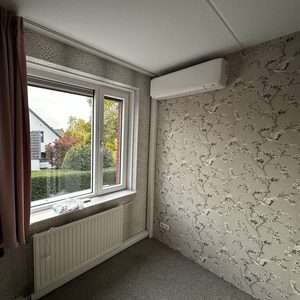 Een wandgemonteerde airconditioningseenheid in een kamer met uitzicht op een tuin.