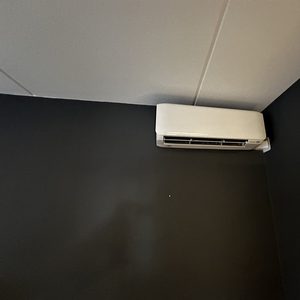 Een wandmodel airconditioningunit is geïnstalleerd op een donkere muur, waarmee koeling en verwarming in de ruimte mogelijk is.