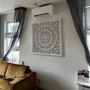 Een wandgemonteerde airconditioningseenheid in een modern interieur met een artistiek wandpaneel eronder.