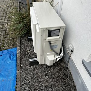 Externe airconditioning unit zichtbaar, geïnstalleerd op een stevige ondergrond. Omgeving met begeleiding door grasplanten.