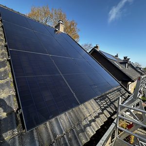 De afbeelding toont een installatie van zonnepanelen op een hellend dak, met een helderblauwe lucht op de achtergrond.