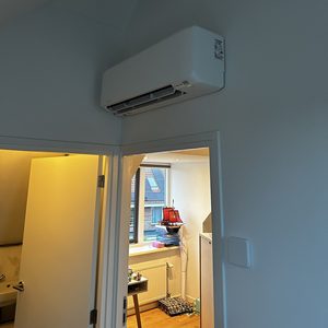 Een wandunit voor airconditioning is geïnstalleerd in de hoek van een kamer, boven een deur.