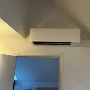 Een wandmontage airconditioningseenheid, geïnstalleerd in een hoek van de kamer voor efficiënte klimaatbeheersing.