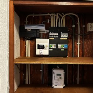De afbeelding toont een meterkast met componenten voor zonnepanelen, waaronder een omvormer en bekabeling.