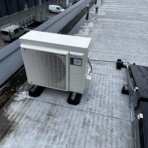 Een geinstalleerde buitenunit van een airconditioning op een plat dak, zichtbaar met naburige structuren op de achtergrond.