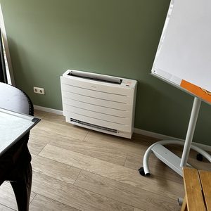 Een wandmontage airconditioningseenheid geplaatst op een groene muur in een interieursetting.
