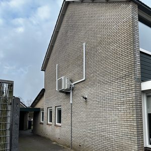 Installatie van een airconditioningseenheid aan de buitenmuur van een woning, met leidingen die naar binnen leiden.