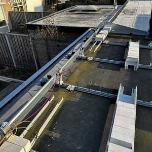 De afbeelding toont een gedeelte van een zonnepaneleninstallatie met montagesystemen en bedrading op een plat dak.