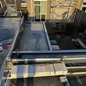 Een deel van het installatieproces voor zonnepanelen op een vlakke dakstructuur, met zichtbare montagematerialen en bekabeling.