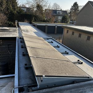 De afbeelding toont een installatie van zonnepanelen op een plat dak, met duidelijk zichtbare zonnepanelen en hun montagesysteem.