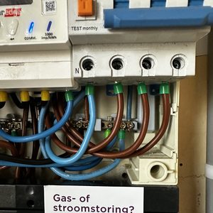 De afbeelding toont de meterkast met bedrading en een informatief lyciet van Liander over stroomstoringen.