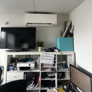 Een wand-airconditioner gepositioneerd boven een bureau in een kantoorruimte voor efficiënte koeling.