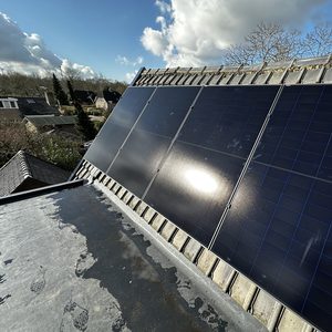 Drie zonnepanelen zijn geïnstalleerd op een hellend dak met een heldere lucht op de achtergrond.