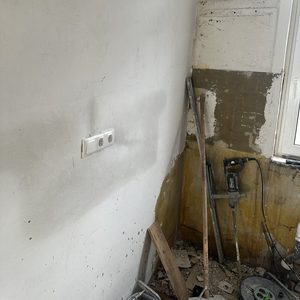 De afbeelding toont een gedeeltelijk gerenoveerde muur met elektrische schakelaars en gereedschap in de buurt van een meterkast-installatie.