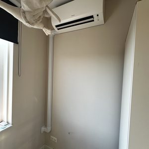 Een wand airconditioner is geïnstalleerd in een interieur, met een bijbehorende afvoerpijp die aan de muur is bevestigd.