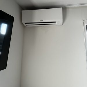 Installatie van een wand-airco unit in een kamer, met een televisie zichtbaar in het kader.