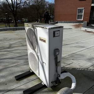 De installatie toont een buitenunit van een airconditioningsysteem, geplaatst op een plat dak met zichtbare aansluitingen.