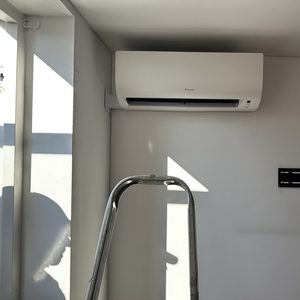 Een muurbevestigde airconditioningseenheid, net geïnstalleerd met een ladder in beeld voor installatieondersteuning.