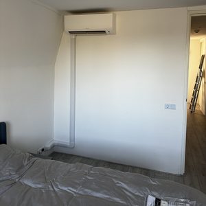 Installatie van een wand-airconditioner in een woonruimte met zichtbare leidingen.