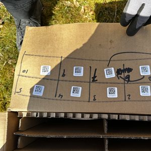 Deze afbeelding toont een doos met zonnepaneelcomponenten en QR-codes voor installatie-instructies.