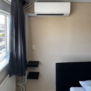Een wandgemonteerde airconditioner is geïnstalleerd, met leidingen die naar de buitenkant lopen, passend in een slaapkameromgeving.