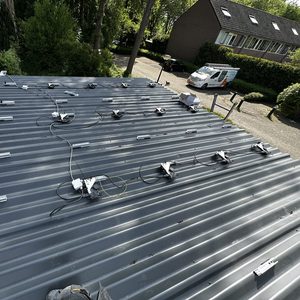 Installatie van zonnepanelen op een metalen dak met bevestigingsrails en kabels voor elektriciteit.