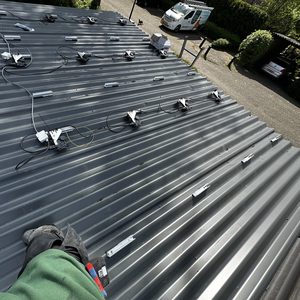 Een zonnepaneelsysteem in installatie op een hellend metalen dak, met meerdere montagesteunen en bedrading zichtbaar.