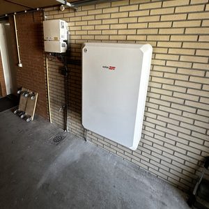 De installatie toont een thuisbatterij geïntegreerd met een omvormer in een garage-achtige ruimte, wat energieopslag in de woning mogelijk maakt.