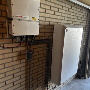 De installatie toont een thuisbatterij met bijbehorende omvormer, gemonteerd aan de muur in een garage-achtige ruimte.