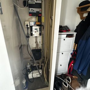 De afbeelding toont een installatie van een airco in een kast, met leidingen en een meterkast zichtbaar.