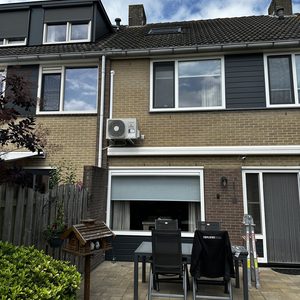 De afbeelding toont een airco-installatie aan de buitenkant van een woning, met een duidelijk zichtbare unit.