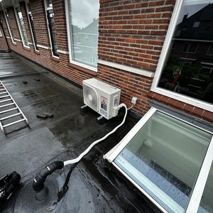 Een buitenunit van een airconditioningsysteem, geïnstalleerd op een plat dak met leidingen verbonden naar binnen.