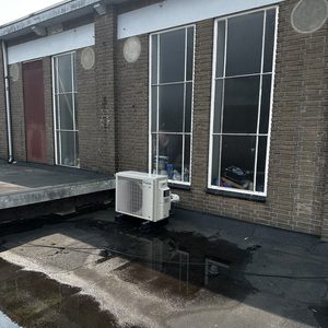 Een airconditioningunit geïnstalleerd buiten, zichtbaar op een plat dak met waterresten eromheen.