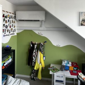Een wandunit voor airconditioning is geïnstalleerd onder het schuine plafond in een kinderkamer.